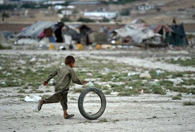 Cậu bé chơi với lốp xe cũ cạnh những túp lều tạm ở ngoài ô thành phố Kabul, Afghanistan.