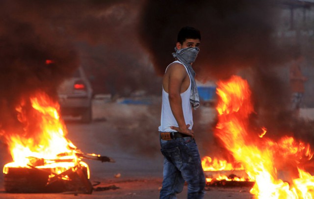 Nam thanh niên người Palestine đứng cạnh những chiếc lốp xe cháy trên đường trong cuộc biểu tình tại ngôi làng Huwara, Bờ Tây.