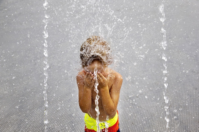 Cậu bé lấy tay che mặt trong khi tắm trong đài phun nước tại công viên Georgetown ở Washington, Mỹ.