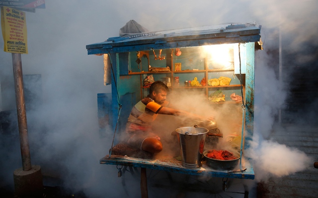 
Người đàn ông bán thuốc trong khi nhân viên y tế phun thuốc diệt muỗi ở Lucknow, Ấn Độ.
