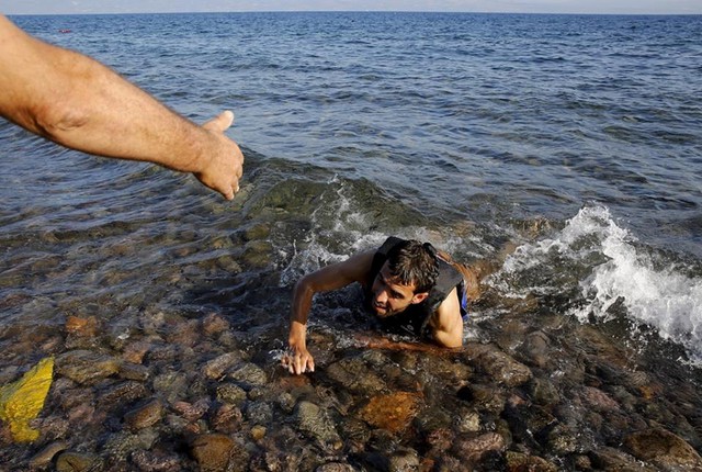 
Một người dân giúp đỡ người tị nạn Syria đang kiệt sức bên bờ biển Lesbos (Hy Lạp) ngày 17/9. (nguồn: CCTVNews)
