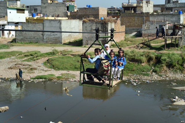 Học sinh đi cáp treo thô sơ để vượt qua dòng suối ô nhiễm trên đường tới trường ở ngoại ô thành phố Islamabad, Pakistan.