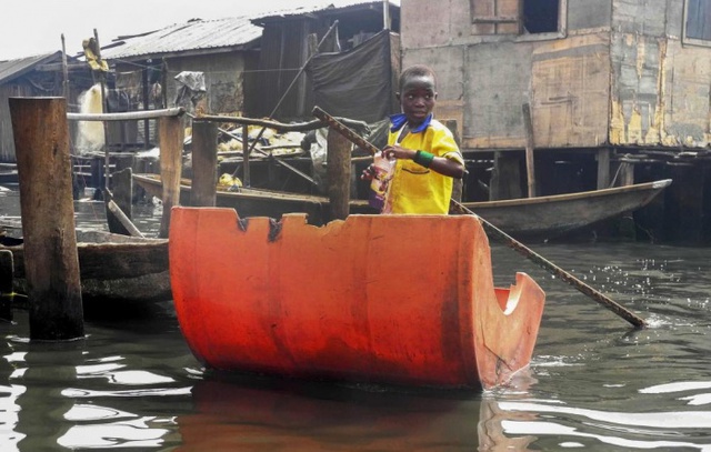 Cậu bé chèo thuyền làm từ nửa chiếc thùng nhựa để tới trường học ở Lagos, Nigeria.