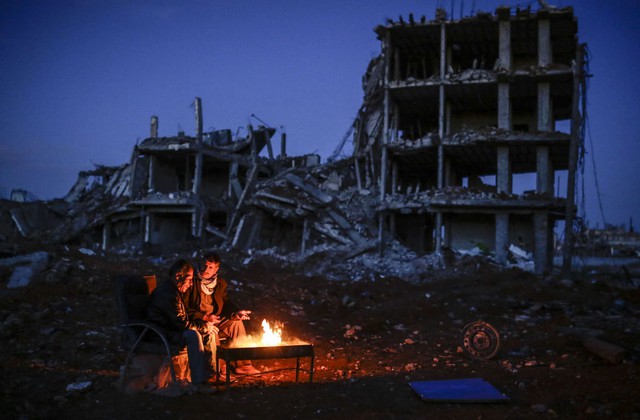 Hai người đàn ông ngồi sưởi ấm quanh một đống lửa gần tòa nhà bị phá hủy ở thị trấn Kobane, Syria.
