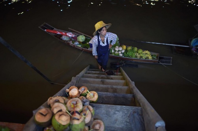 Một người bán trái cây đứng chờ khách mua cạnh thuyền của mình dưới dòng kênh Amphawa ở Samut Songkhram, Thái Lan.