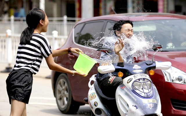 Cô gái té nước vào một người đi xe điện trên đường trong lễ hội té nước mừng năm mới ở tỉnh Vân Nam, Trung Quốc.