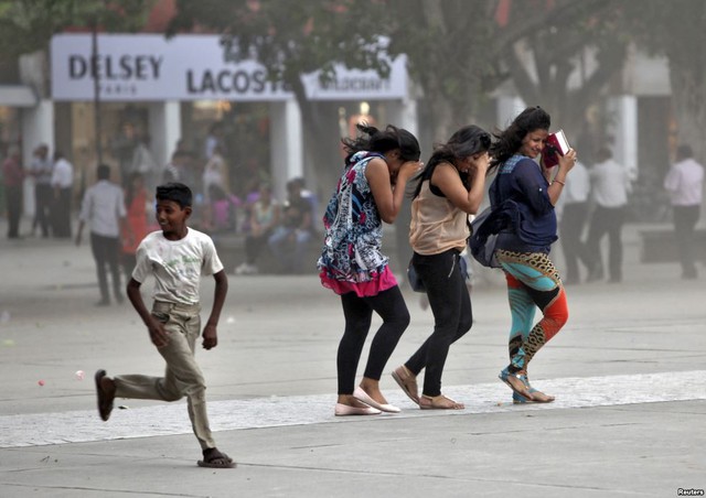 Cậu bé chạy gần các cô gái đang che mặt khỏi bão cát trước một trung tâm thương mại ở Chandigarh, Ấn Độ.