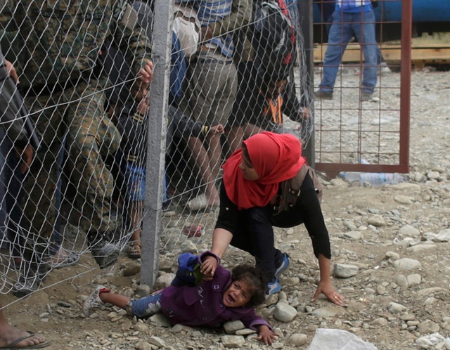 Em bé bị ngã khóc thét khi những người di cư cố vượt qua một hàng rào để lên một chuyến tàu tại Gevgelija, Macedonia gần biên giới với Hy Lạp.