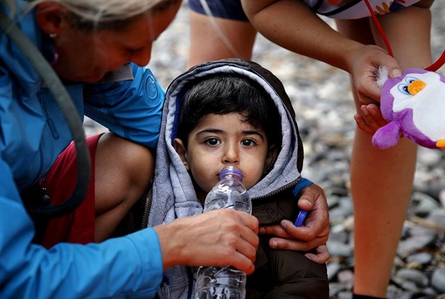 
Những người tình nguyện cho em bé tị nạn Syria uống nước và đồ chơi sau khi gia đình em kiệt sức vì chuyến đi vượt biển Aegean từ bờ biển Thổ Nhĩ Kỳ ngày 22/9. (Nguồn: CCTVNews)
