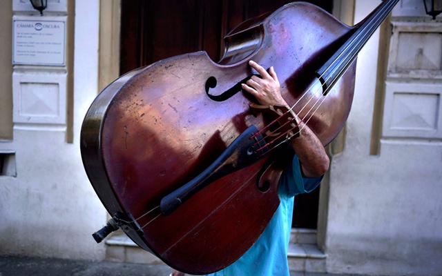 Nhạc công mang cây đàn công-bat trên đường tới nơi làm việc ở Havana, Cuba.