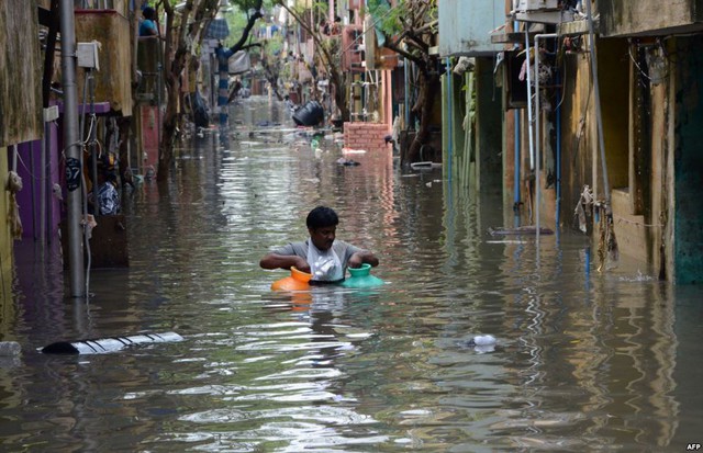 Người đàn ông mang theo những chiếc bình khi lội trên đường ngập lụt tại thành phố Chennai, Ấn Độ.