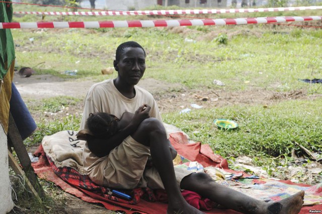 James Flomo, bị nghi nhiễm virus Ebola, ngồi bế con nhỏ trong khu cách ly tại Monrovia, Liberia. Vơ của anh Flomo tử vong trước đó do nhiễm loại virus chết người này.