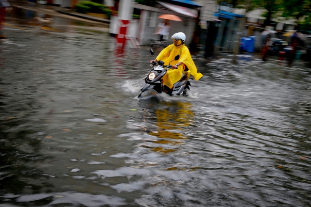 Người đàn ông lái xe máy đi qua đường phố ngập lụt ở Bangkok, Thái Lan.