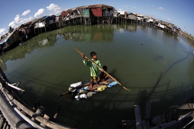 Một cậu bé chèo chiếc bè tạm cạnh khu ổ chuột ở Bacoor, Philippines.