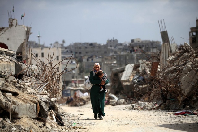 Người phụ nữ Palestine bế con đi qua những ngôi nhà bị phá hủy trong cuộc không kích của quân đội Israel nhằm vào thành phố Gaza.