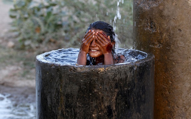 Bé gái tắm mát dưới dòng nước chảy ra từ đường ống nước bị vỡ ở ngoại ô Ahmedabad, Ấn Độ.