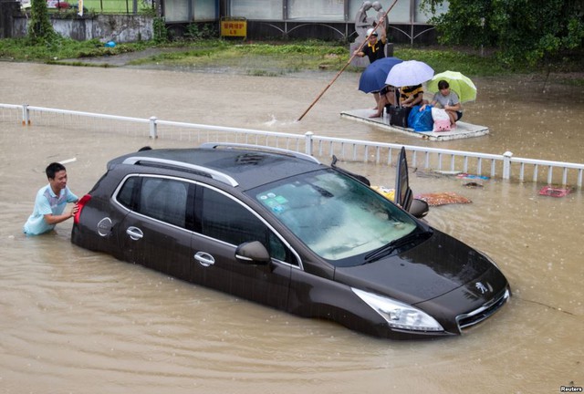 Mọi người đẩy một chiếc xe mắc kẹt trên đường phố ngập lụt sau khi siêu bão Soudelor quét qua thành phố Phúc Châu, Trung Quốc.