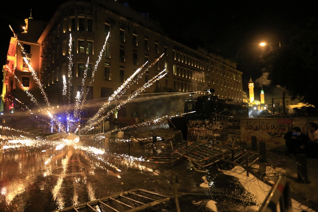 Người biểu tình ném pháo trong khi cảnh sát chống bạo động phun vòi rồng trong cuộc đụng độ trên đường phố ở Beirut, Li Băng.