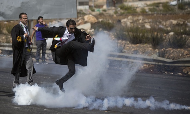 
Một luật sư người Palestine đá lựu đạn hơi cay trở lại phía binh sĩ Israel trong cuộc biểu tình gần thành phố Ramallah, Bờ Tây.

