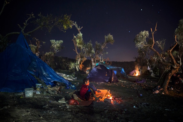 
Cậu bé di cư người Afghanistan ngồi sưởi ấm bên đống lửa tại ngôi làng Moria trên đảo Lesbos, Hi Lạp.
