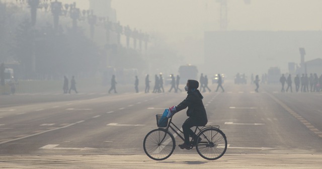 Người phụ nữ Trung Quốc đeo khẩu trang kín mít đạp xe dọc theo một con phố gần quảng trường Thiên An Môn khi lần thứ 2 Bắc Kinh phải ban hành cảnh báo đỏ về mức độ ô nhiễm không khí và khói bụi.