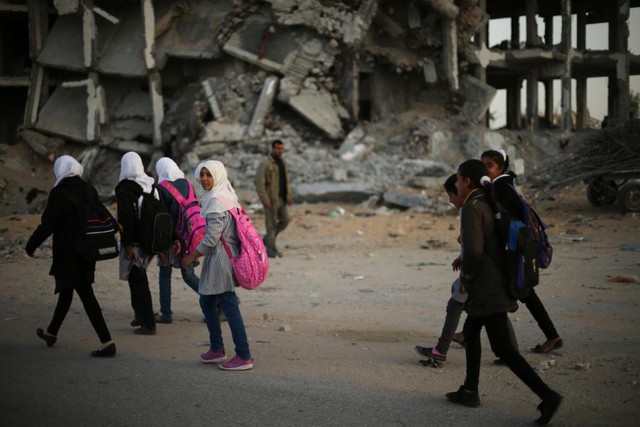 Các nữ sinh người Palestine đi qua tòa nhà chung cư bị phá hủy trong cuộc không kích của Israel vào thị trấn Biet Lahiya, Dải Gaza.