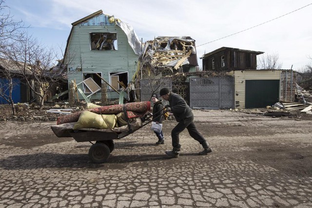 Người đàn ông đẩy xe chở đồ đạc qua các tòa nhà bị tàn phá bởi đạn pháo ở thị trấn Debaltseve, Ukraine.
