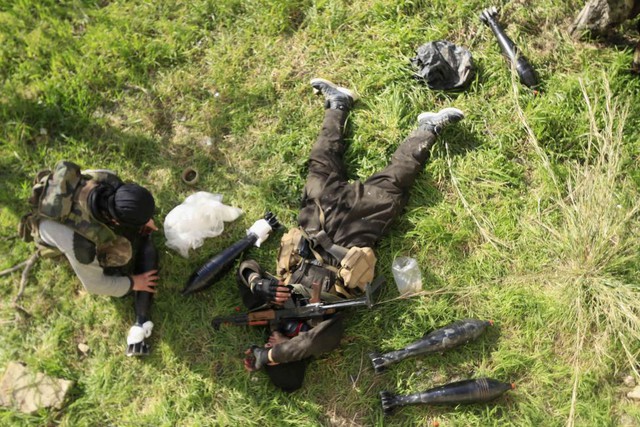 Một chiến binh phiến quân Syria nằm nghị cạnh chiến hữu đang chuẩn bị đạn cối để phóng nhằm vào quân đội chính phủ ở ngoại ô thị trấn Doreen, tỉnh Latakia.