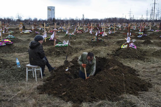 Người phụ nữ ngồi cạnh chồng đang đào huyệt tại một nghĩa trang ở Donetsk, miền đông Ukraine.