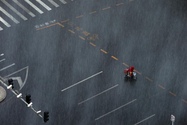 Người đàn ông dắt chiếc xe đạp điện đi dưới mưa lớn tại thành phố Bắc Kinh, Trung Quốc.