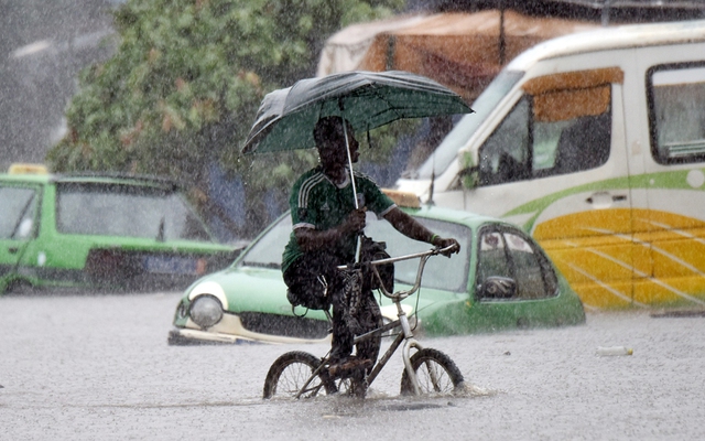 Người đàn ông đạp xe dưới mưa lớn trên đường phố ngập lụt ở thành phố Abidjan, Bờ Biển Ngà.