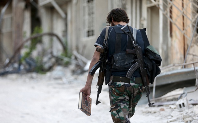 Chiến binh phiến quân Syria cầm quyển kinh Koran của đạo Hồi khi đi bộ dọc một đường phố ở ngoại ô thành phố Damascus.
