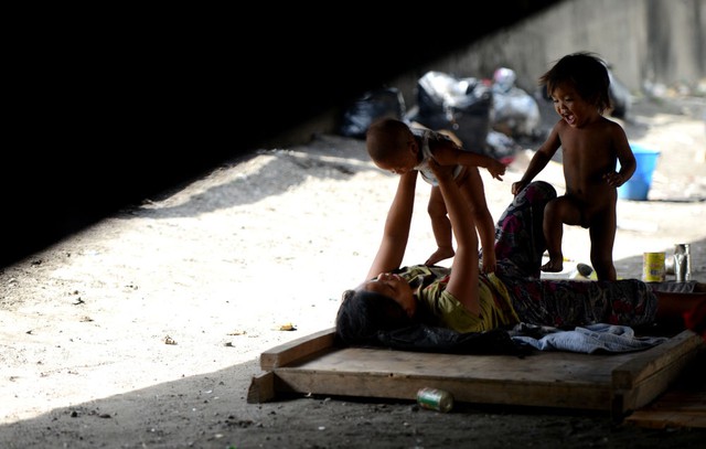Một phụ nữ vô gia cư chơi với những đứa con của mình dười gầm cầm vượt ở Manila, Philippines.