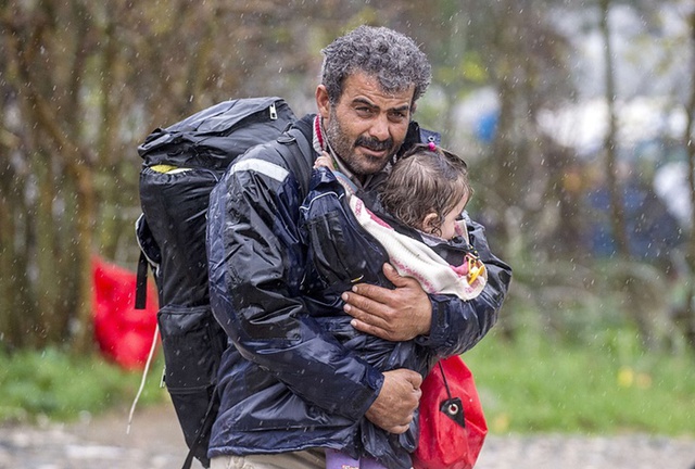 
Người đàn ông di cư cố gắng che mưa cho con nhỏ sau khi vượt qua biên giới Hy Lạp sang Gevgelija, Macedonia.
