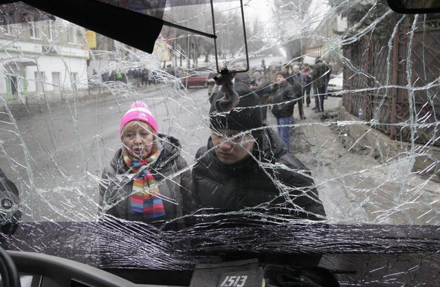 Mọi người nhìn qua kính trước của chiếc xe bus bị trúng đạn pháo ở Donetsk, Ukraine.