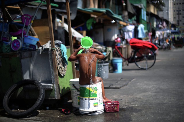 Cậu bé tắm bên ngoài nhà mình tại một khu ổ chuột ở thành phố Manila, Philippines.