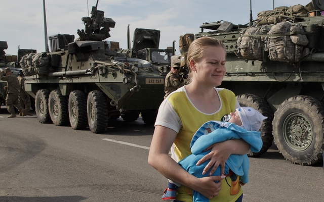 Một bà mẹ bế con nhỏ đi qua hàng dài phương tiện bọc thép quân đội Mỹ đỗ trên đường ở Ploiesti, Romania.