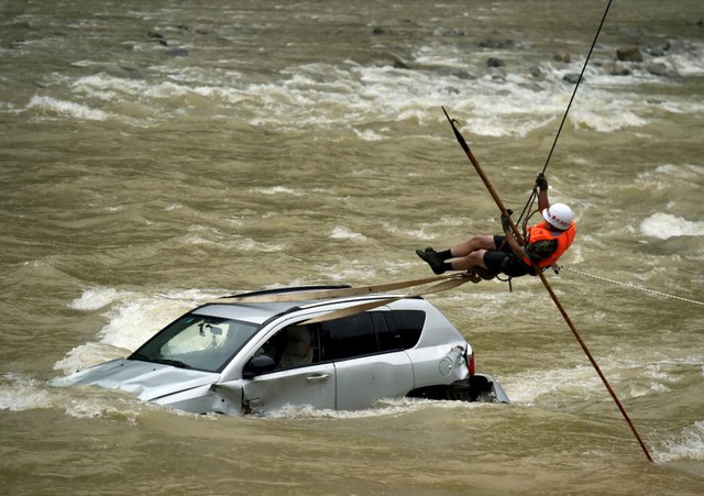 Nhân viên cứu hộ cố gắng kéo chiếc xe ô tô mắc kẹt trong dòng nước lũ chảy xiết ở thành phố Trùng Khánh, Trung Quốc.