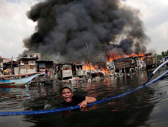 Người đàn ông bơi thoát khỏi đám cháy tại một khu ổ chuột ở thành phố Paranaque, Philippines.