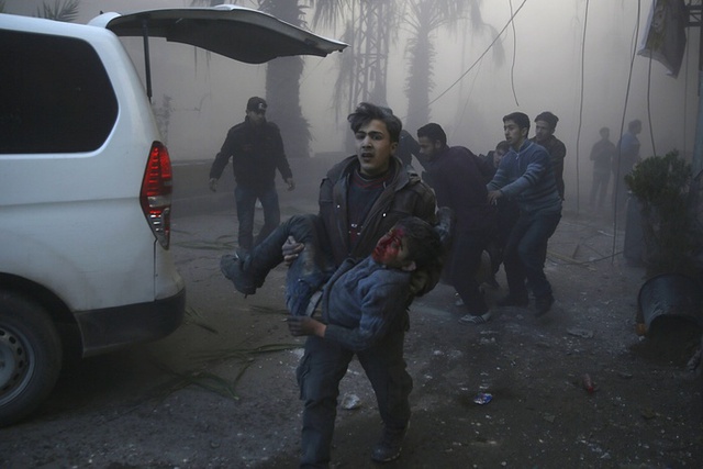 Người đàn ông bế một cậu bé bị thương trong cuộc không kích nhằm vào thị trấn Hamouria gần thủ đô Damascus, Syria.