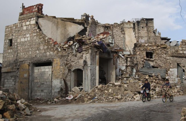 Các cậu bé đạp xe qua tòa nhà bị phá hủy bởi bom đạn trong cuộc nội chiến kéo dài ở Aleppo, Syria.