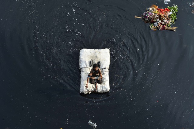 Cậu bé sử dụng bè tạm để di chuyển trên sông Yamuna ở New Delhi, Ấn Độ.