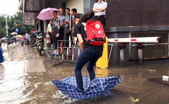 Cô gái đứng trên chiếc ô lộn ngược để vượt qua một đoàn đường ngập nước ở thành phố Phúc Châu, Trung Quốc.