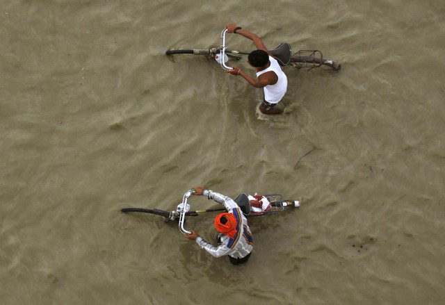 Những người đàn ông dắt xe đạp trên bờ sông Hằng ngập nước ở thành phố Allahabad, Ấn Độ.