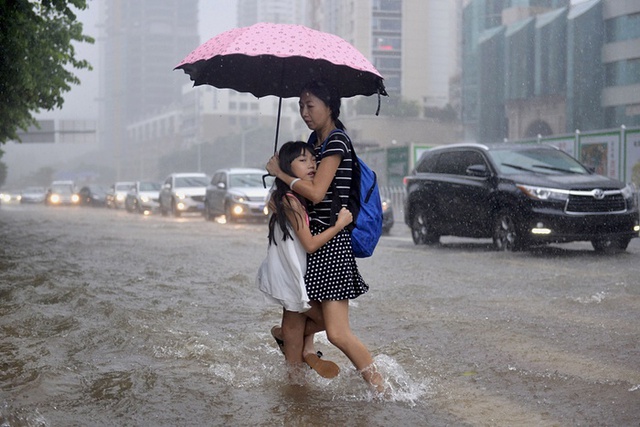 Bé gái bám chặt vào mẹ khi di chuyển trên đường phố ngập lụt ở thành phố Thâm Quyến, Trung Quốc.