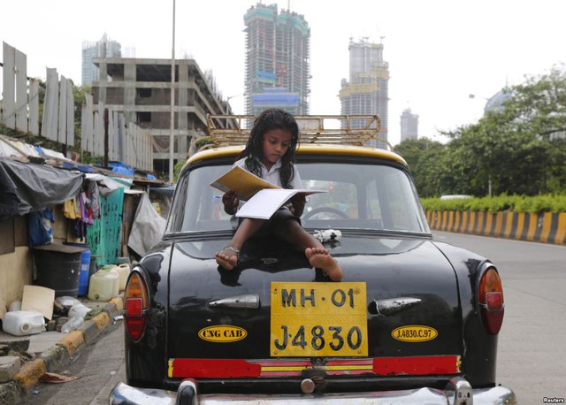 Bé gái ngồi học trên xe taxi bên ngoài ngôi nhà ổ chuột ở thành phố Mumbai, Ấn Độ.