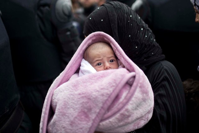 Một phụ nữ di cư bế con nhỏ đi qua hàng rào cảnh sát tại trung tâm tiếp nhận người tị nạn ở Opatovac, Croatia.