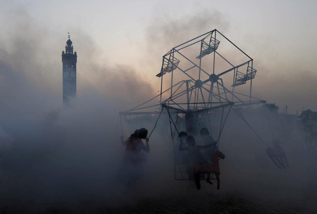 Trẻ em chơi đua quay trong khi nhân viên y tế phun thuốc diệt muỗi tại một khu ổ chuột ở Lucknow, Ấn Độ.
