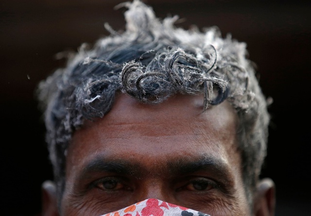 Những sợi bông phủ trắng đầu một công nhân gia công chăn từ vật liệu tái chế ở Kathmandu, Nepal.