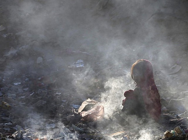 Bé gái ngồi giữa bãi rác đang cháy âm ỉ tại thành phố Kabul, Afghanistan.